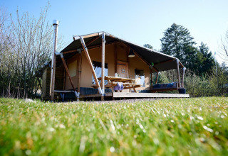 Tienda Safari Cottage en Camping Vossenberg, Países Bajos, con porche, mesa de picnic y césped verde.