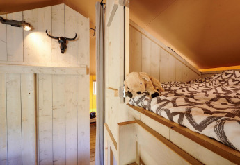 Vista interna della Safari tent Cottage con letto rialzato, peluche e arredo rustico in legno al Camping Vossenberg.