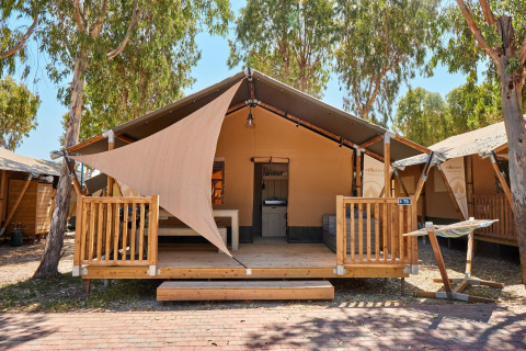 Tenda safari presso Villatent Outback con veranda in legno, amaca e alberi ombreggianti sullo sfondo.