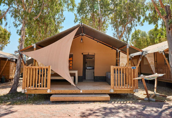 Tenda safari presso Villatent Outback con veranda in legno, amaca e alberi ombreggianti sullo sfondo.