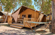 Safari tent Villatent Outback met houten veranda, hangmat en bomen op een zonnige kampeerlocatie.