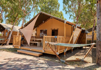 Tienda safari Villatent Outback con terraza de madera y hamaca entre árboles en un camping soleado.