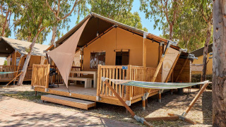 Tienda safari Villatent Outback con terraza de madera y hamaca entre árboles en un camping soleado.