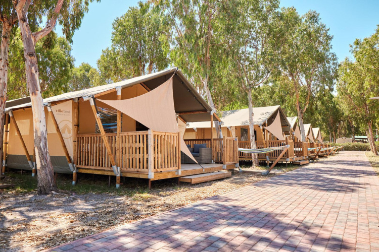 Tiendas safari con terrazas de madera en Villatent Outback, rodeadas de árboles y un camino pavimentado.