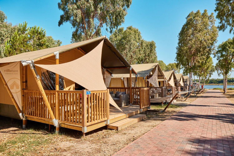 Row of safari tents called Villatent Outback by a walkway, surrounded by trees and natural scenery.