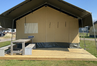 Safaritent bij Holiday Park Duinhoeve in Nederland met houten terras en picknickbank op het gras.
