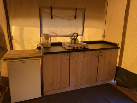 Cocina de una tienda safari en Holiday Park Duinhoeve, Países Bajos, con fogón, tetera y refrigerador.