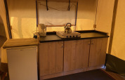 Cocina de una tienda safari en Holiday Park Duinhoeve, Países Bajos, con fogón, tetera y refrigerador.