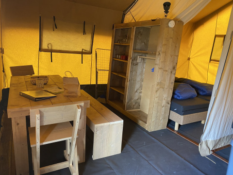 Interior de una tienda safari en Holiday Park Duinhoeve, Países Bajos, con muebles de madera y cama.
