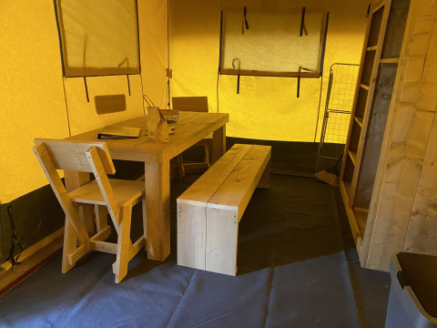 Interior de una tienda safari con mesa, banco y sillas de madera en Holiday Park Duinhoeve, Países Bajos.