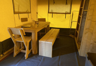 Interior de una tienda safari con mesa, banco y sillas de madera en Holiday Park Duinhoeve, Países Bajos.