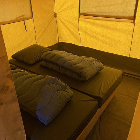 Binnenkant van safaritent met twee bedden en beddengoed bij Holiday Park Duinhoeve in Nederland, warm licht.