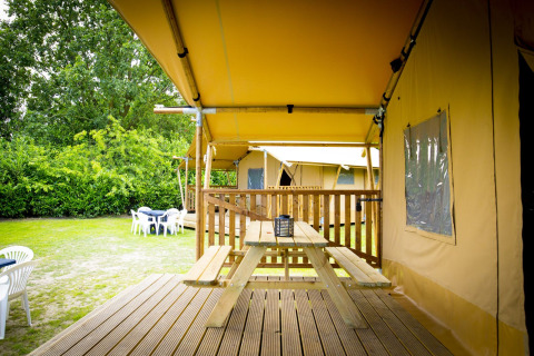Glamping Deluxe type 1 safaritent bij Holiday Park Duinhoeve in Nederland, met houten veranda en picknicktafel.