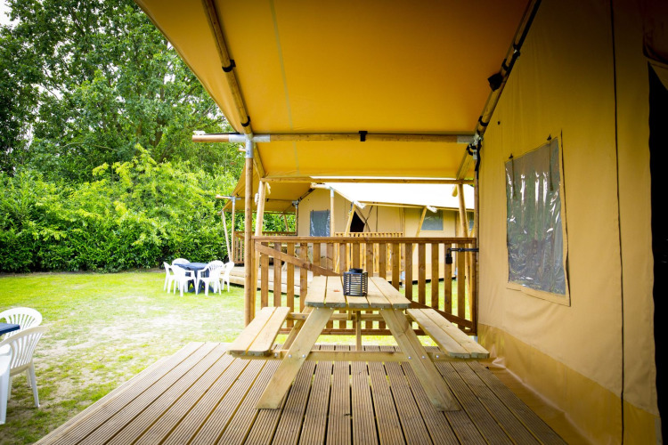 Glamping Deluxe type 1 safaritent bij Holiday Park Duinhoeve in Nederland, met houten veranda en picknicktafel.