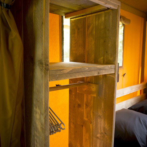 Indvendig visning af et safari telt på Holiday Park Duinhoeve med træhylder og tøjstativer.