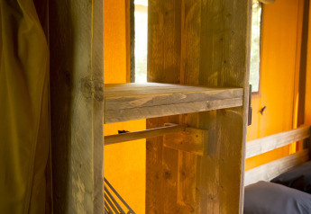 Vista interior de una tienda safari en Holiday Park Duinhoeve con estantes de madera y perchas.