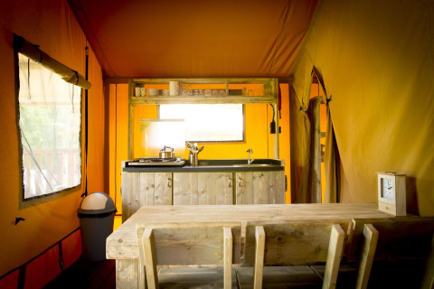 Vista interior de una tienda safari glamping con cocina y mesa en Holiday Park Duinhoeve, Países Bajos.