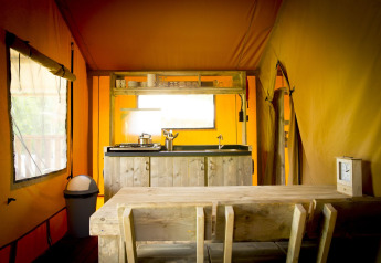 Vista interior de una tienda safari glamping con cocina y mesa en Holiday Park Duinhoeve, Países Bajos.