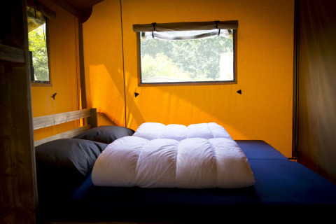 Interior de una tienda Glamping Deluxe en Holiday Park Duinhoeve, Países Bajos, con cama y ventana.