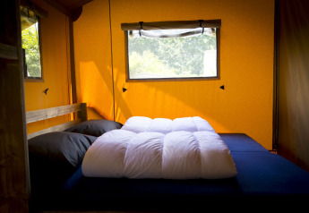 Interior de una tienda Glamping Deluxe en Holiday Park Duinhoeve, Países Bajos, con cama y ventana.
