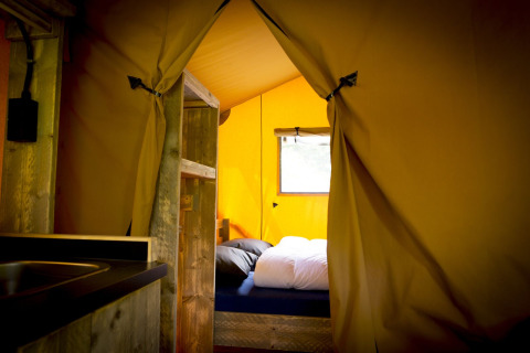 Interior de una tienda safari Glamping Deluxe tipo 1 en Holiday Park Duinhoeve, Países Bajos, con cama visible.
