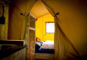 Interior de una tienda safari Glamping Deluxe tipo 1 en Holiday Park Duinhoeve, Países Bajos, con cama visible.