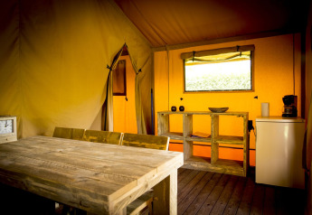 Interior de la tienda safari Glamping Deluxe tipo 1 en Holiday Park Duinhoeve, Países Bajos, con mesa de madera.