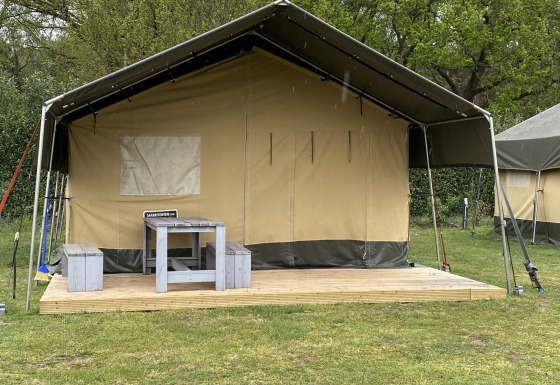 Tente safari XL au Holiday Park Duinhoeve aux Pays-Bas avec terrasse en bois, table et bancs à l’avant.