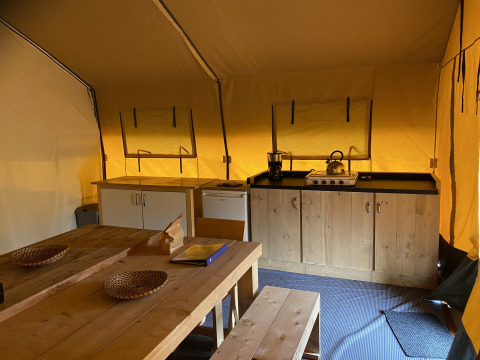 Interior de la Safari tent XL en Holiday Park Duinhoeve, Países Bajos, con cocina, mesa y bancos de madera.