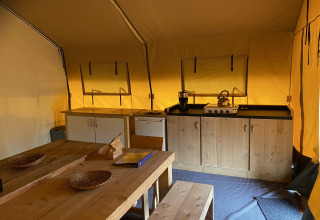 Interior of Safari tent XL at Holiday Park Duinhoeve in the Netherlands, featuring kitchen and wooden table.