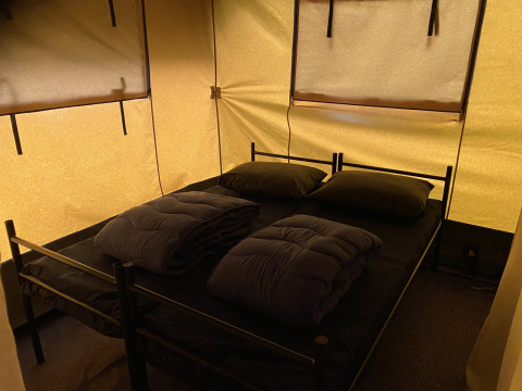 Área para dormir en la tienda Safari XL en Holiday Park Duinhoeve, Países Bajos, con dos camas y mantas.