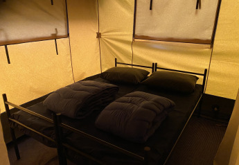 Área para dormir en la tienda Safari XL en Holiday Park Duinhoeve, Países Bajos, con dos camas y mantas.