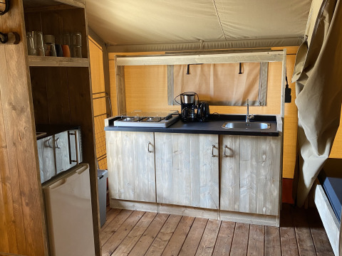 Zona de cocina en Glamping Deluxe tipo 2 en Holiday Park Duinhoeve con armarios de madera y estufa.