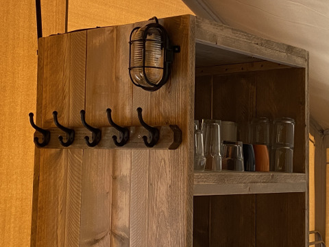 Estante de madera con ganchos, lámpara y vasos en Glamping Deluxe tipo 2 en Holiday Park Duinhoeve, Países Bajos.