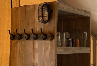 Houten plank met haken, lamp en glazen in Glamping Deluxe type 2 bij Holiday Park Duinhoeve, Nederland.