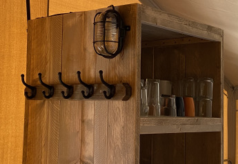 Estante de madera con ganchos, lámpara y vasos en Glamping Deluxe tipo 2 en Holiday Park Duinhoeve, Países Bajos.