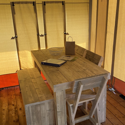 Mesa de madera con banco y silla en el interior de una tienda Glamping Deluxe tipo 2 en Holiday Park Duinhoeve, Países Bajos.