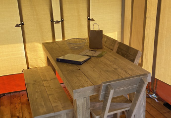 Mesa de madera con banco y silla en el interior de una tienda Glamping Deluxe tipo 2 en Holiday Park Duinhoeve, Países Bajos.