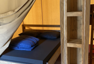 Vista interior de un lodge Glamping Deluxe tipo 2 con muebles y cama de madera en Holiday Park Duinhoeve.