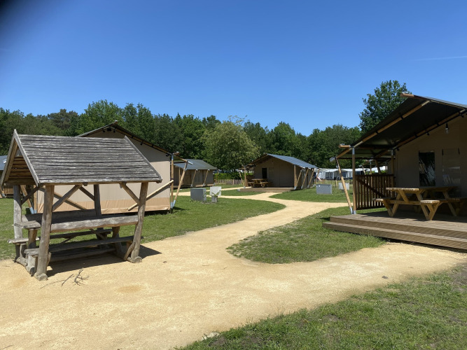 Glamping Deluxe type 2 lodge op Holiday Park Duinhoeve, Nederland, met safaritenten en picknickbanken buiten.