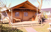 Tienda Safari DeLuxe en Camping Vossenberg, Países Bajos, con terraza de madera y asientos exteriores.