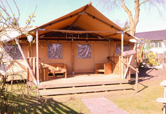 Safari tent DeLuxe at Camping Vossenberg in the Netherlands, featuring a wooden porch and outdoor seating.
