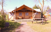 Tienda safari DeLuxe en Camping Vossenberg, Países Bajos, con terraza de madera y mesa de picnic afuera.