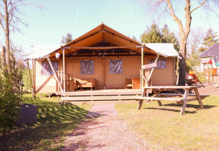 Safari tent DeLuxe at Camping Vossenberg in the Netherlands, with wooden porch and picnic table outside.