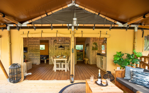 Vista interior de la tienda safari DeLuxe en Camping Vossenberg, Países Bajos, con comedor y zona de estar.