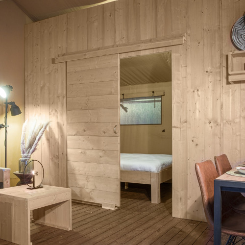 Vista interior de la tienda Safari DeLuxe en Camping Vossenberg, Países Bajos, con paredes y muebles de madera.