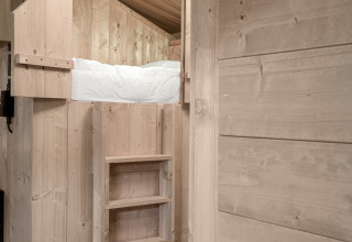 Interior view of a raised bed with ladder in the Safari tent DeLuxe at Camping Vossenberg, Netherlands.