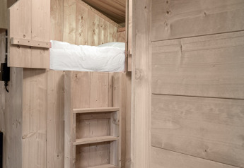 Vista interior de una cama elevada con escalera en la Safari tent DeLuxe del Camping Vossenberg, Países Bajos.