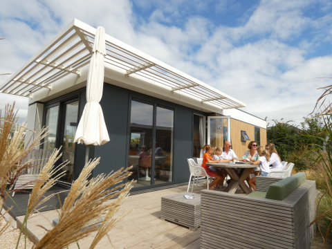 Family enjoying outdoor meal at a modern Dune Lodge Family in Camping Zonneweelde, the Netherlands.