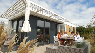 Familie genießt eine Mahlzeit draußen an der Dune Lodge Family auf Camping Zonneweelde in den Niederlanden.